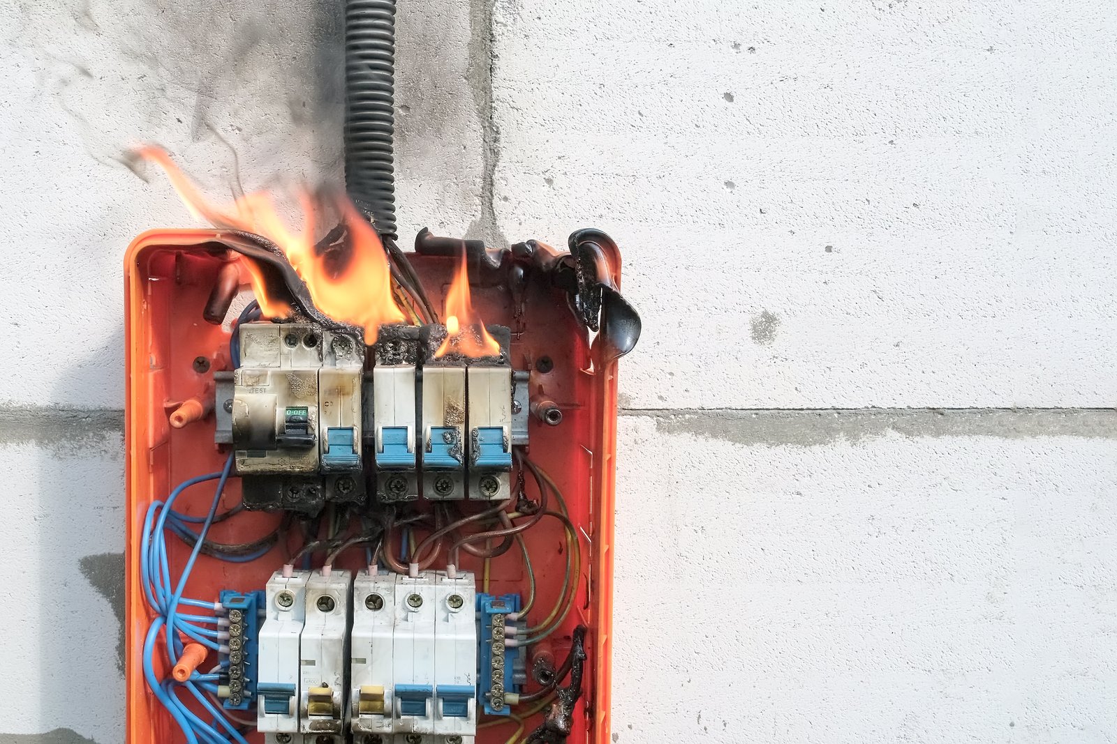 Electrical panel on fire with visible flames and melted components, highlighting a serious fire hazard.