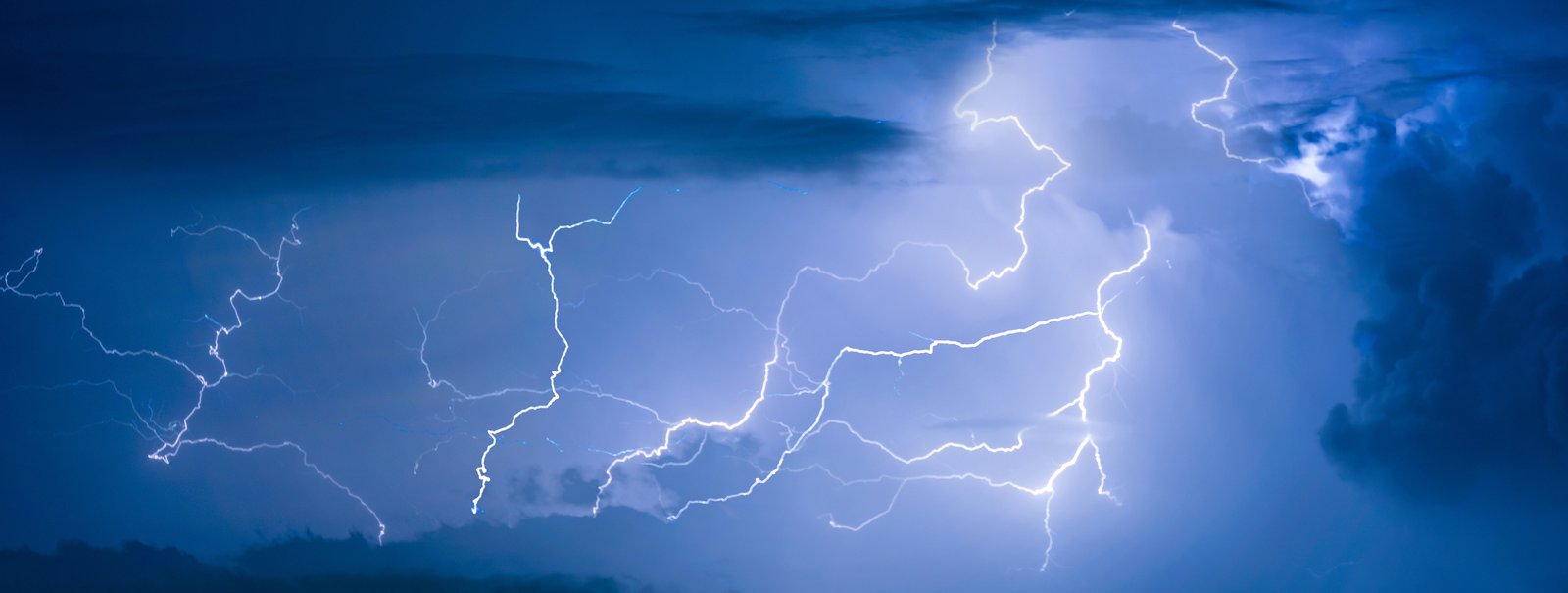 Multiple lightning bolts illuminating the night sky with dark storm clouds in the background.