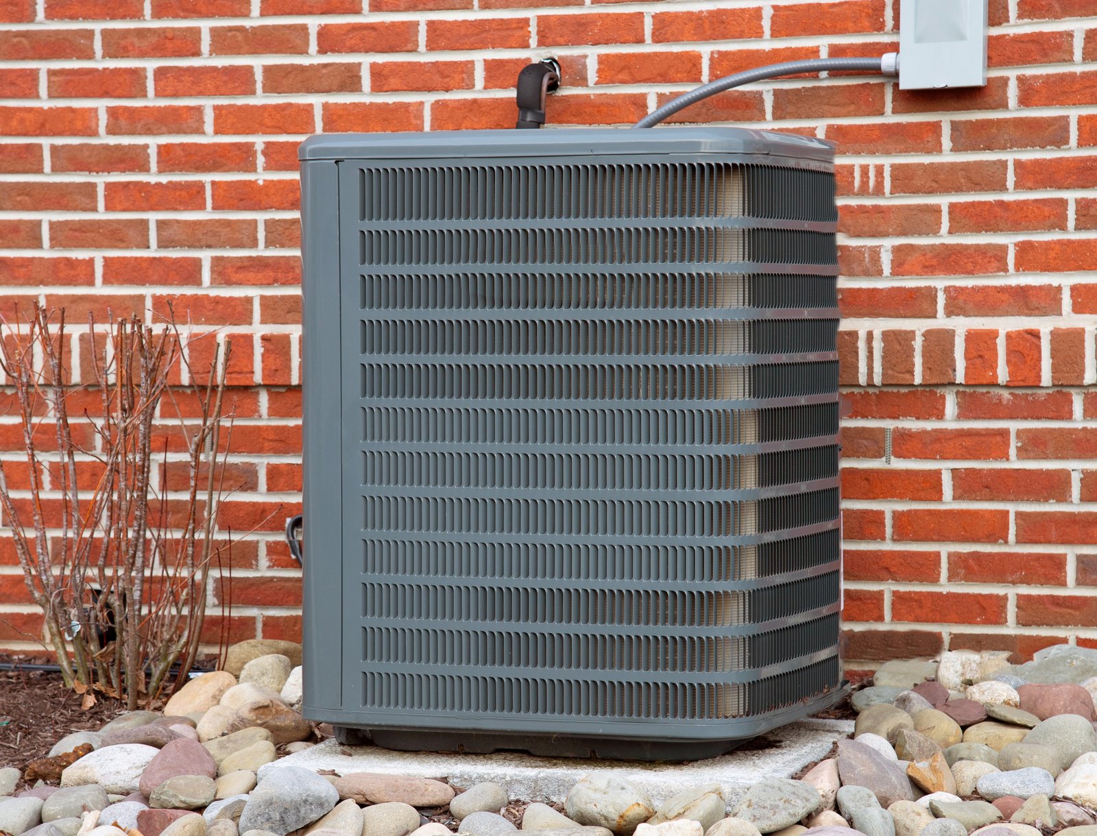 An outdoor HVAC unit installed against a brick wall, providing heating and cooling for a residential building.